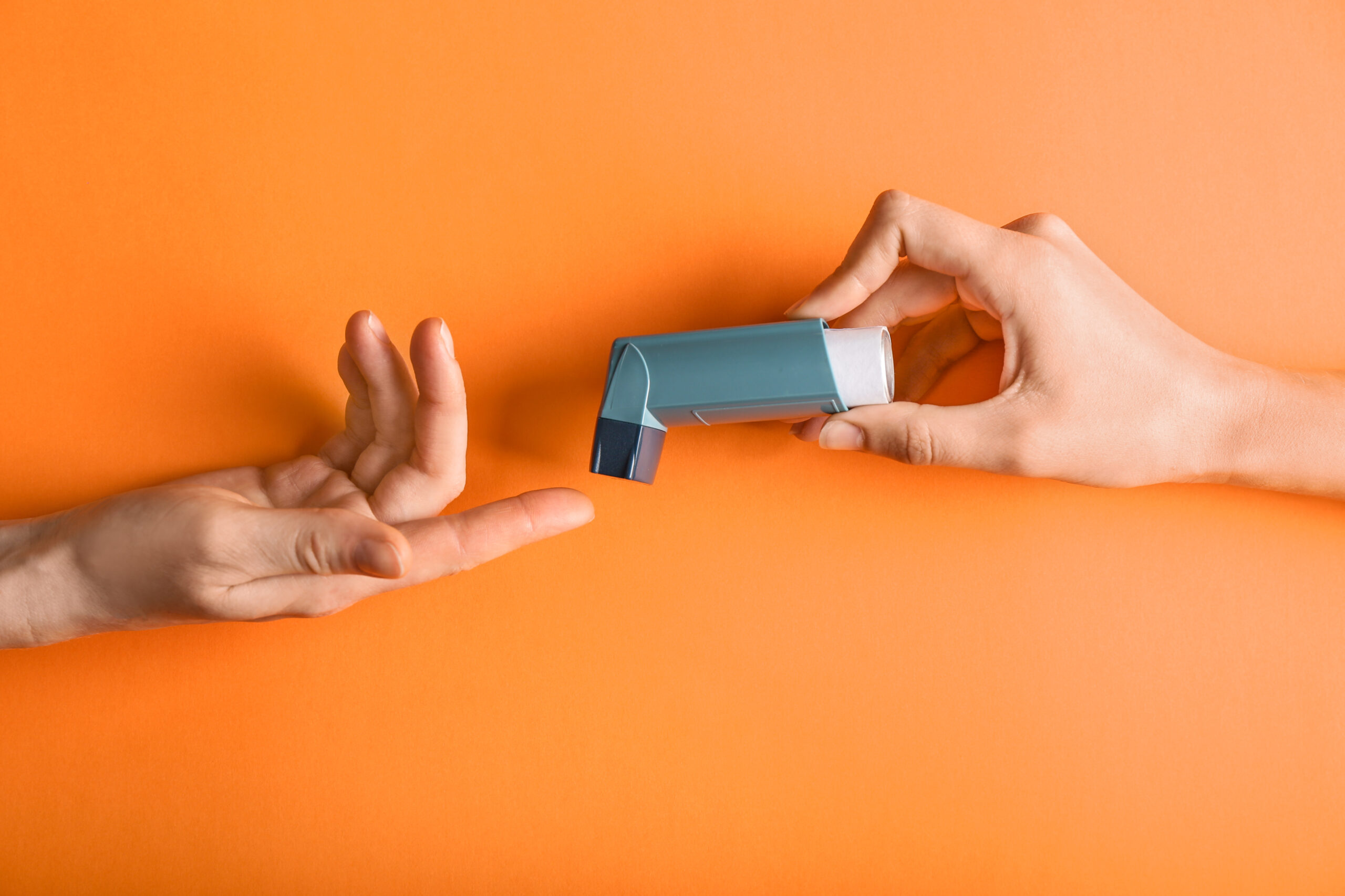 Female hands with inhaler against asthma on color background