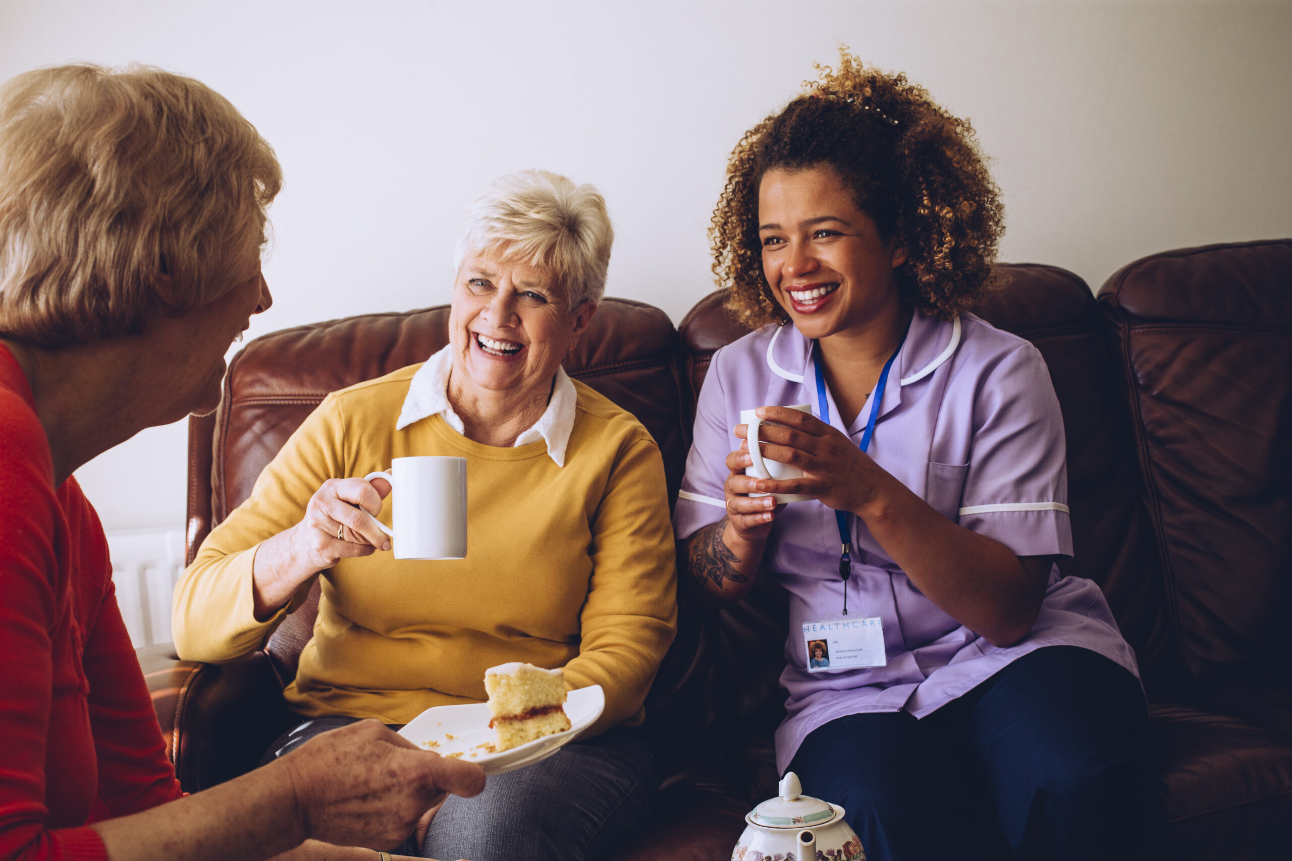 Elderly Carer Sitting With Two Of Her Patients having tea